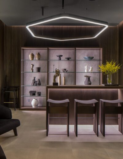 Modern living room with geometric lighting, dark-toned furniture, and a backlit display shelf.